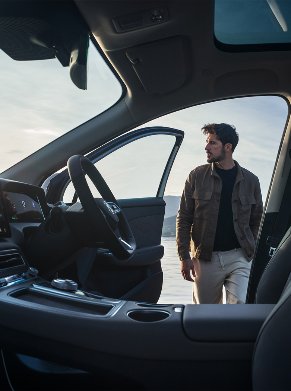 Man standing beside an open car door, interior view with visible dashboard and seats.