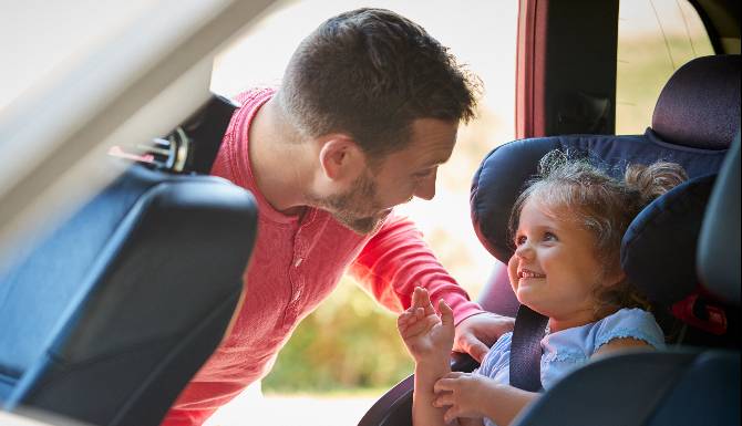 Father Securing Daughter Into Car Seat